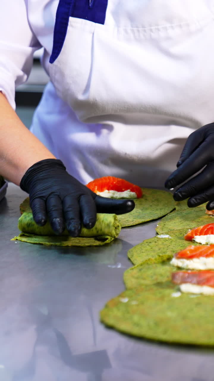 Thin pancakes with herbs are rolled with salmon and cottage cheese. Cook in black gloves puts the fish stuffing into crepes. Vertical video