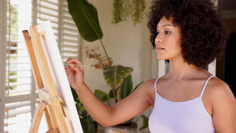 painting on canvas, woman creating artwork in home studio with plants