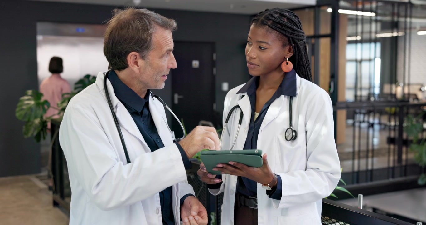 Two Doctors Discussing Medical Data on a Tablet in a Hospital Corridor