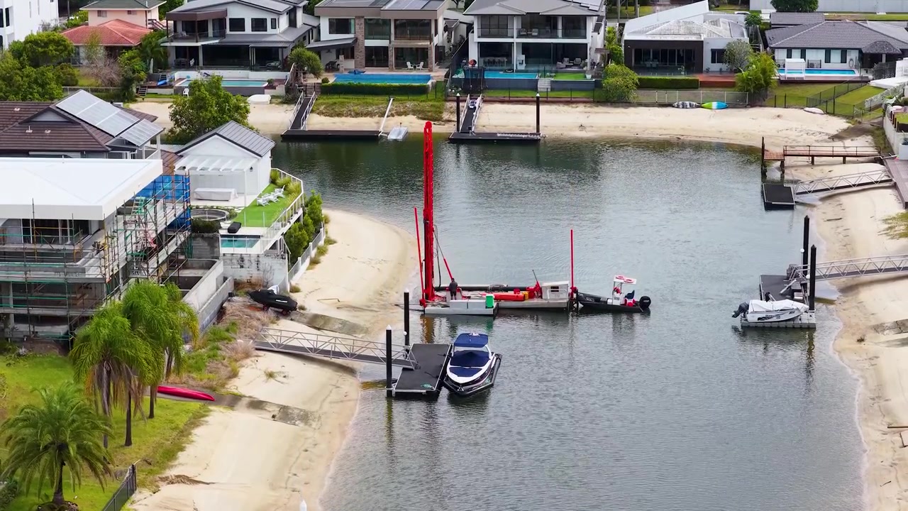 Un dron captura una plataforma de pilotaje roja operando en un canal acuático residencial de lujo frente al mar.