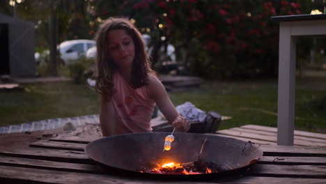 cute young girl toasting marshmallows on a skewer over a fire