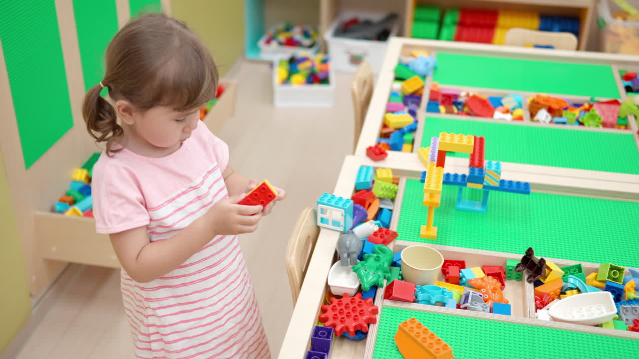 백인 아이 작은 소녀가 놀이실에서 벽돌이나 블록을 만드는 장난감 건설기를 연결하는 놀이를 하고 있습니다.
