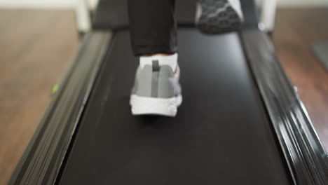 woman runs on treadmill at home closeup. athletic lady in sports shoes jogs exercising on trainer machine in house slow motion. domestic fitness