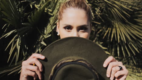 stylish young woman covering mouth with hat outdoors.