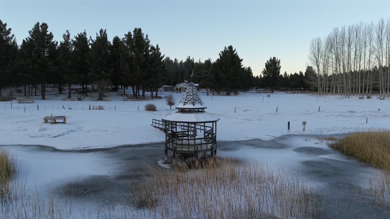 Drone orbiting snowy pier on frozen Laguna La Zeta with lonely woman gazing in silence