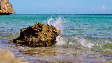 4k 60fps deslizador lento de roca siendo golpeado por pequeñas olas en aguas poco profundas, entrada tropical de la bahía del caribe