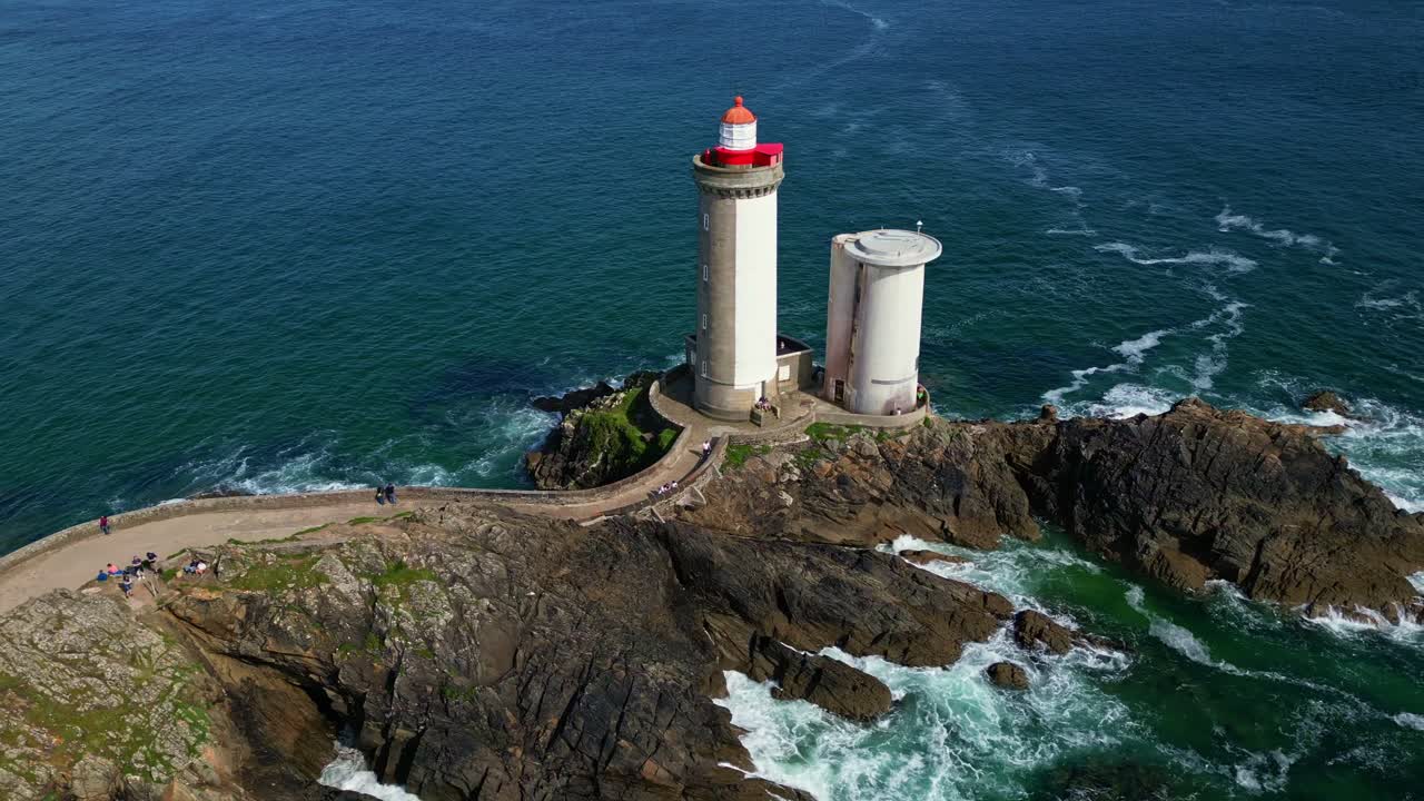 Drone tilt-down and lateral shot over Petit Minou lighthouse in Brittany, starting at the stone bridge and moving past the lighthouse along the cliffs and ocean waves. Plouzané, France
