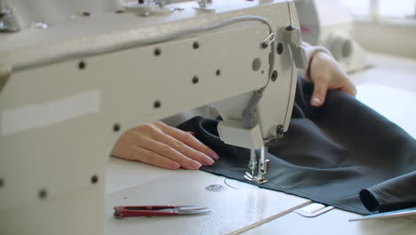 a female hand pushes material through a sewing machine