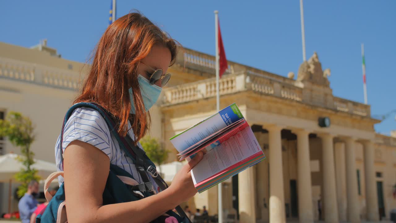 Mladá cestovatelka na dovolené ve Vallettě na Maltě před Palácem velmistrů kontroluje svého průvodce pro reference.