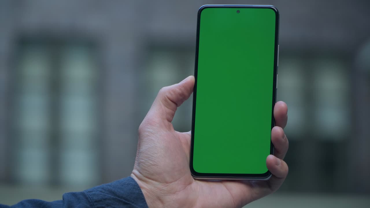 4K Primo piano della mano di un uomo che tiene uno smartphone con schermo verde per strada in città