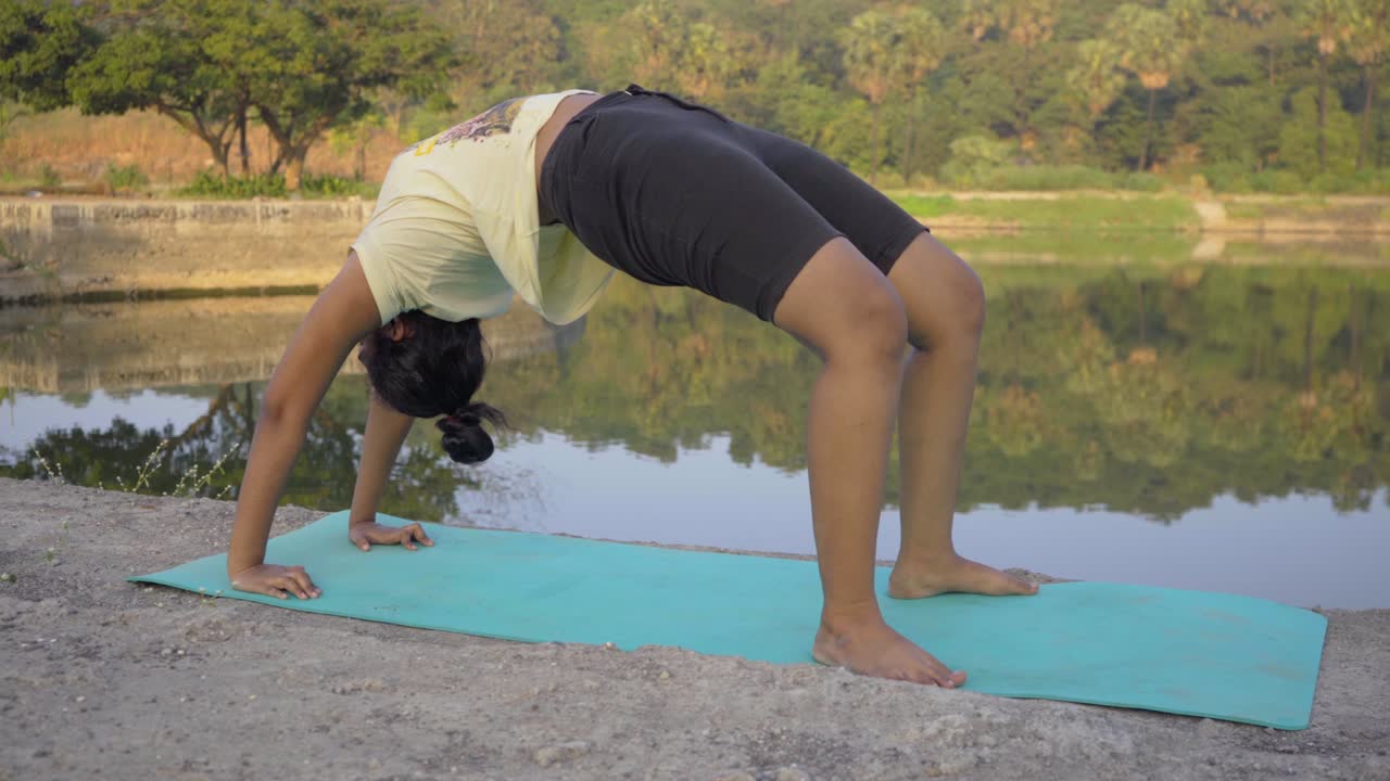 niña india haciendo pose de arco hacia arriba urdhva dhanurasana pose de yoga junto al lago