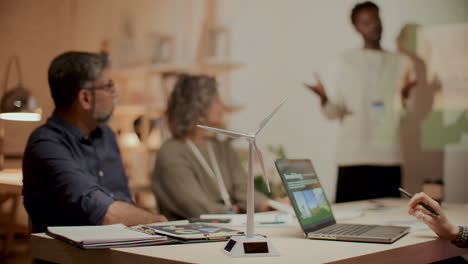 equipo escuchando la presentación en la mesa con modelo de turbina eólica y portátil