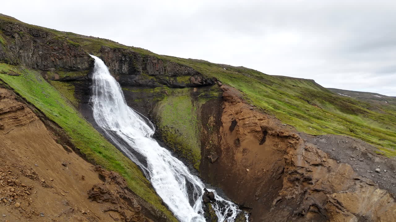 Aerial view of a huge waterfall in Austurland Iceland, showing powerful cascading water, surrounding cliffs, and dramatic Icelandic terrain