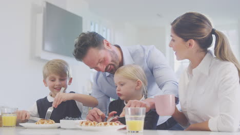 children wearing school uniform in kitchen eating breakfast waffles as parents get ready for work