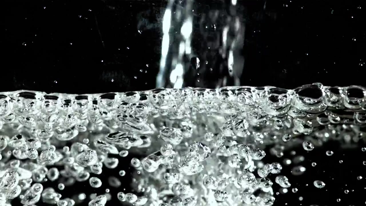 Gros plan d'eau claire versée créant des bulles sur fond noir