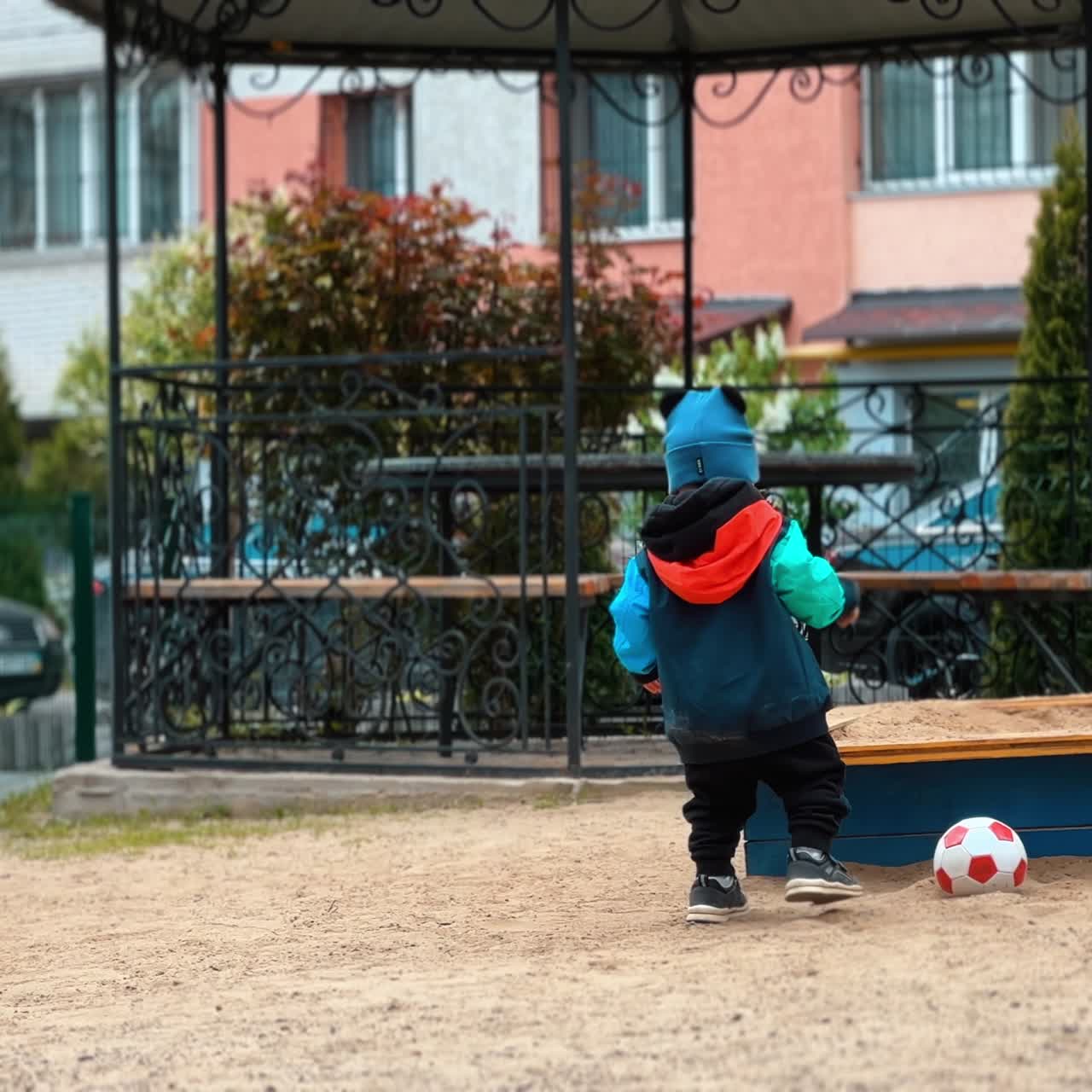 Cute little boy is interested in sand on the playground. Kid takes a handful of sand and throws it