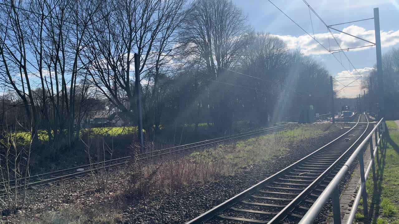 vías de tren vacías con un pequeño trozo de barandillas verdes y grises en primer plano y árboles en el fondo