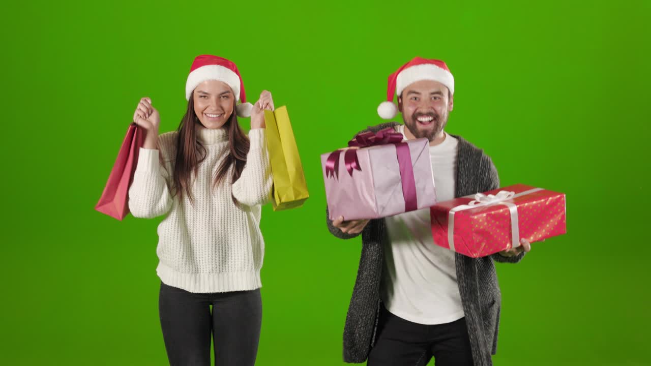 Cheerful couple in santa hats dancing with presents and bags