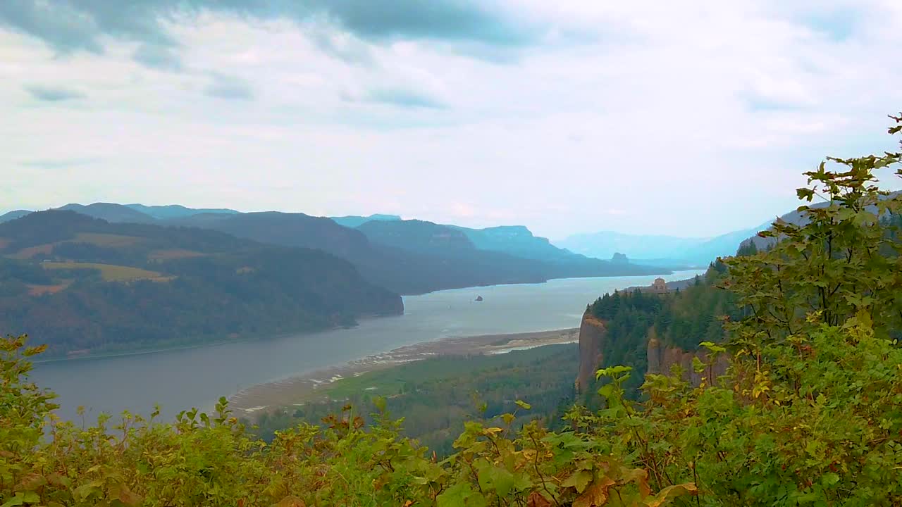 HD Boom up with autumn colored hedges in foreground and the Vista House on a cliff in the distance overlooking the Columbia River with mostly cloudy sky take three