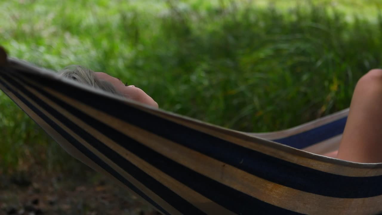 una mujer relajándose en una hamaca de rayas azules y blancas meciéndose en el viento