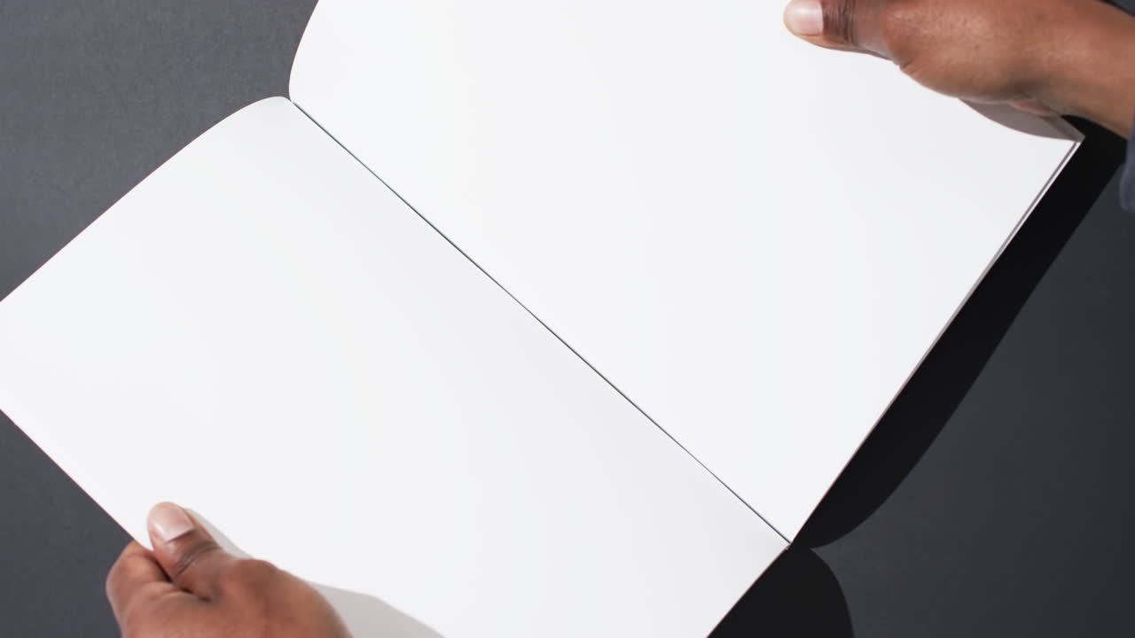 Video of hand of african american man holding book with blank pages, copy space on black background