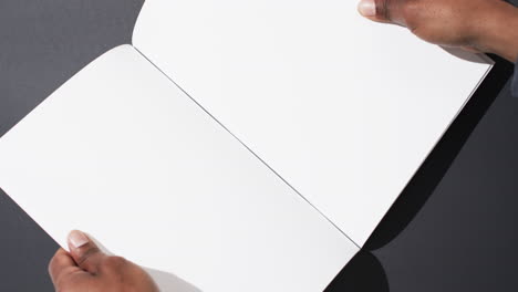 video of hand of african american man holding book with blank pages, copy space on black background