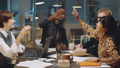 colleagues speaking and high fiving at night business meeting