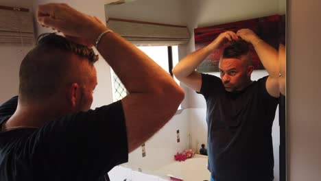 man-styling-his-grey-hair-in-the-mirror-in-the-morning,-Licjed-back-and-looking-good,-combing-hair-with-his-fingers-comb-and-a-brush