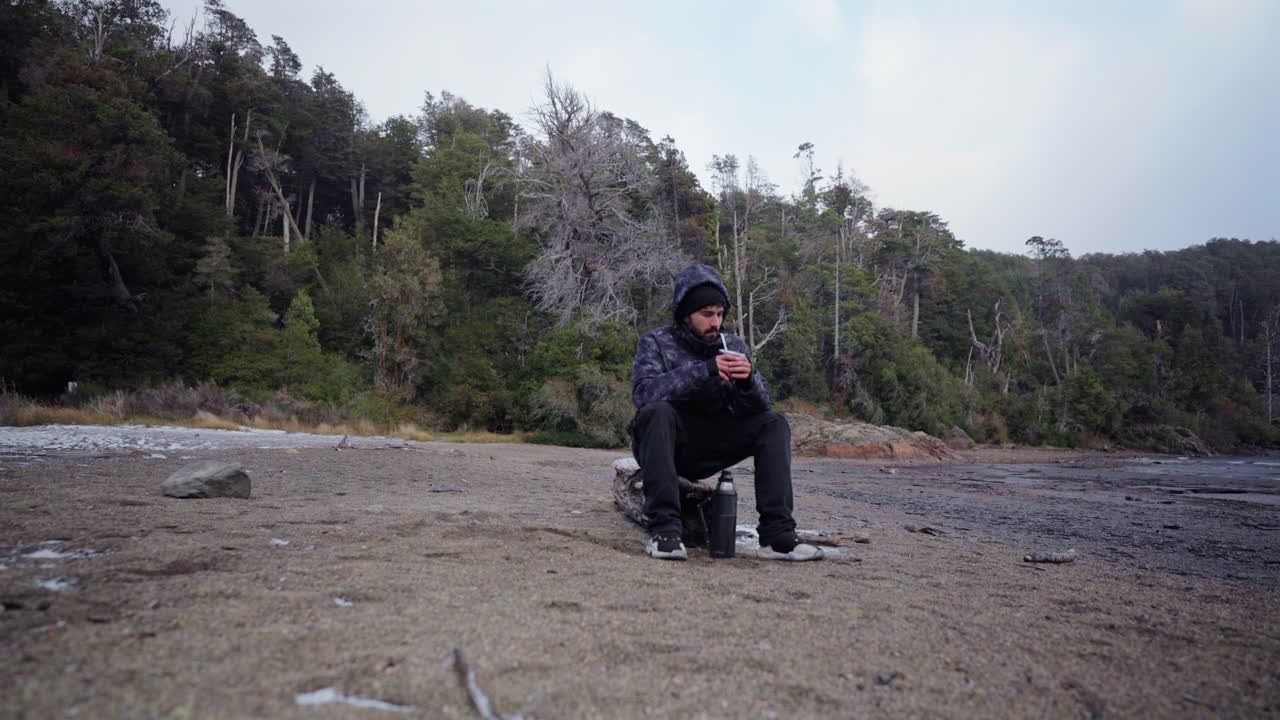 Lonely person sitting on log drinking mate on exotic beach in winter