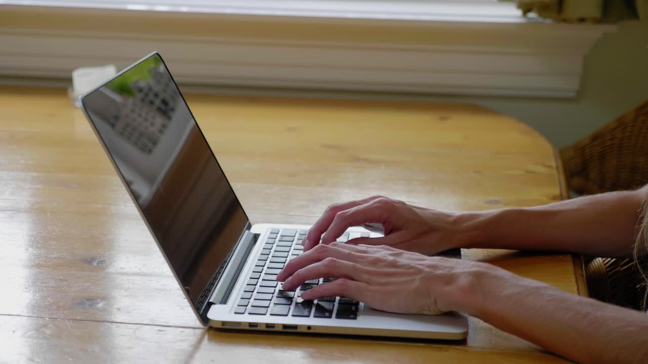 Female hands type on laptop on wooden table at home, close-up, pan