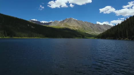 AERIAL:-Drone-flies-towards-Colorado-mountain-over-blue-lake-surrounded-by-evergreen-trees