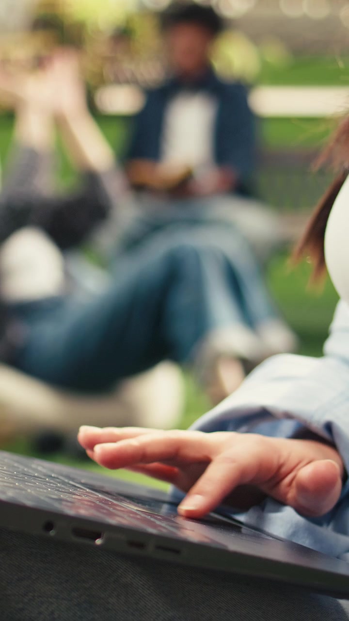 Vertical Video Close up of woman typing on laptop while sitting on grass in modern campus