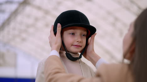 mother helping daughter put on riding helmet