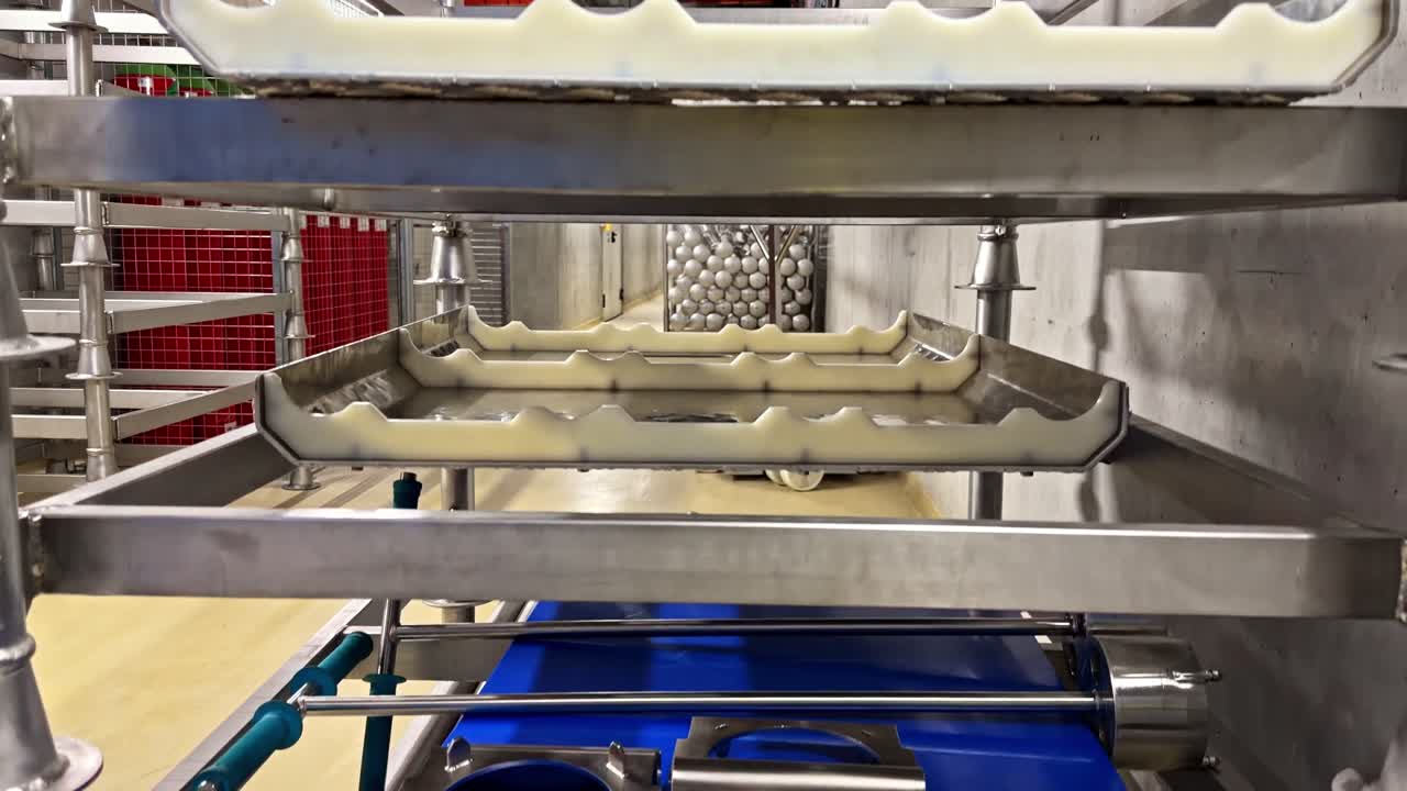 Crane down camera movement inside industrial food factory revealing stainless steel trays water baths pipes and hygienic processing equipment