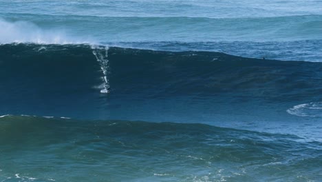 slow motion of a big wave surfer riding a monster wave between mountains in nazaré, portugal