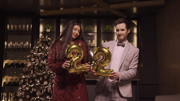 Woman And Man Wearing Elegant Clothes Holding Balloons With The Numbers 22 While Dancing In New Year's Party 1