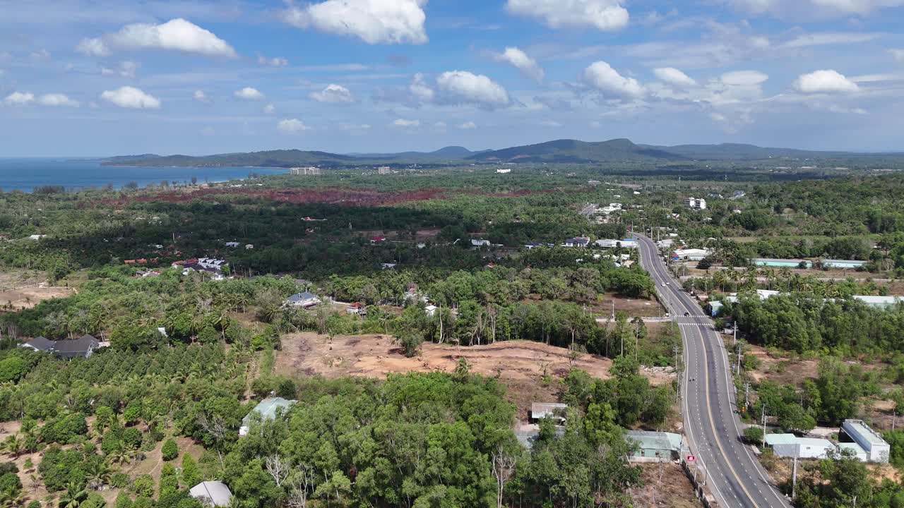 Aerial footage shows a road with reduced traffic, greenery on either side, and residents visible at intervals, creating a calm street. Passing clouds moves, and their shadows play across the road