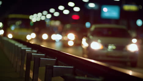 City-highway-guardrail-at-night-closeup.-Cars-silhouettes-driving-on-road.