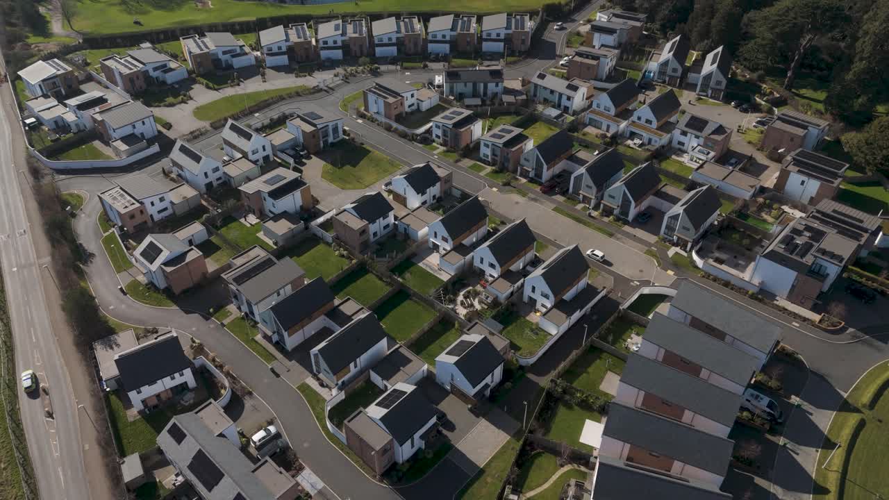 Aerial view of grid-style estate of detached and semi-detached solar homes with steep roofs, garages and tree borders emphasising modern eco suburbia