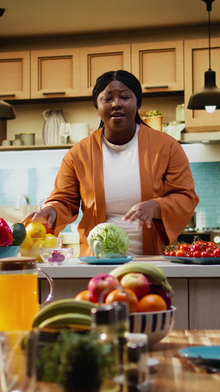 Video verticale: cuoca donna di colore che registra un video tutorial di cucina al bancone della cucina