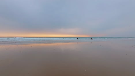 group-of-surfers-carry-colorful-longboards-at-lowtide,-beautiful-sunset-sky