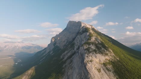 aerial dolly in of steep hill covered in green pine tree forest revealing canadian rockies at banff national park, alberta, canada