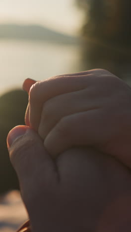 los amantes se toman de la mano sentados al atardecer en primer plano. el novio disfruta de la atmósfera romántica de la cita con la novia en la orilla del río juntos. momento conmovedor