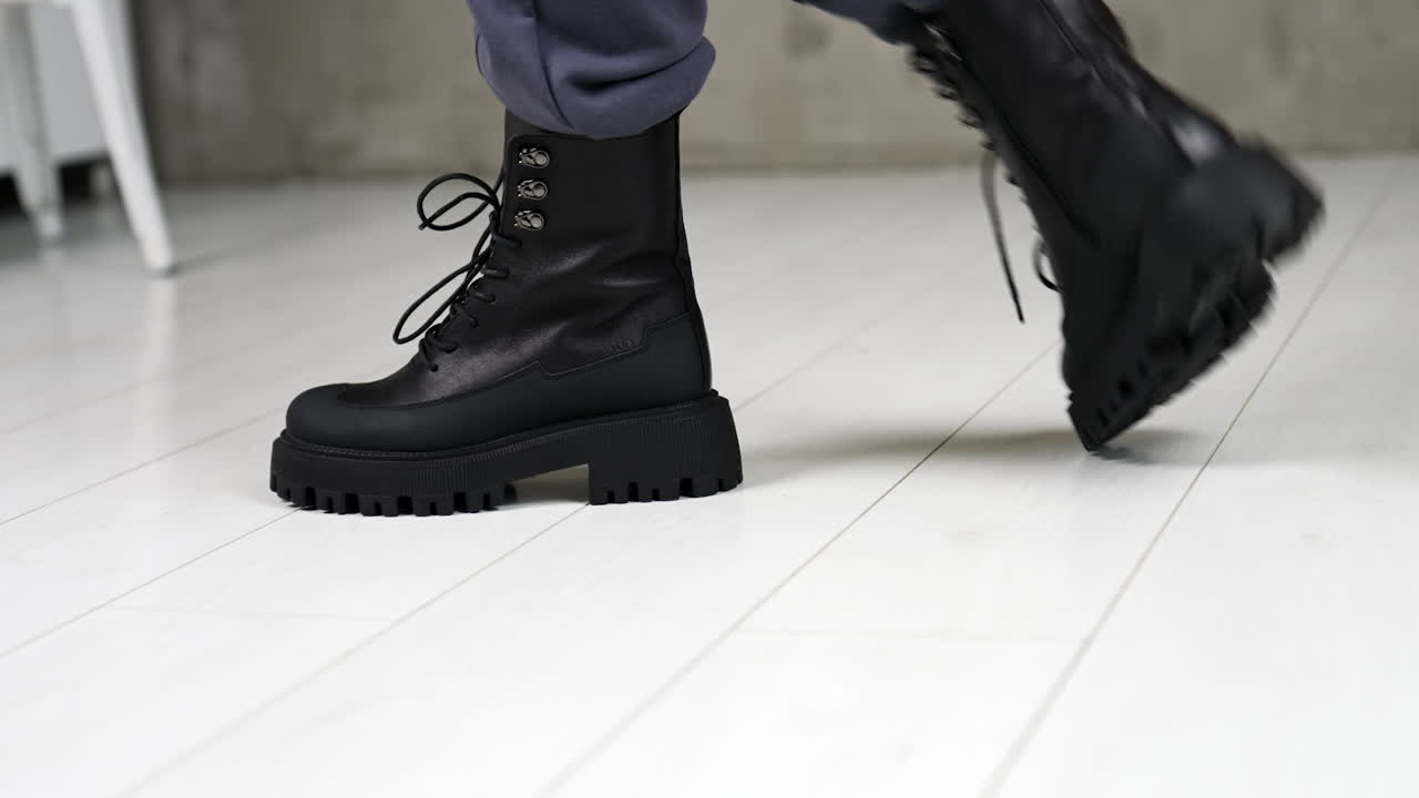 Model demonstrating the fashionable black leather boots with laces. Footwear presentation in light studio. Close up.