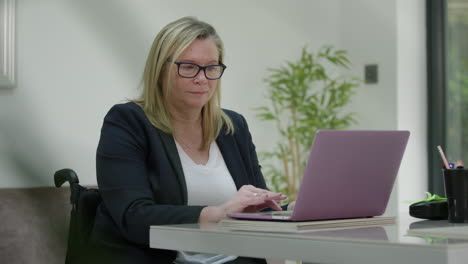 woman in wheelchair working in home office, peering behind plant