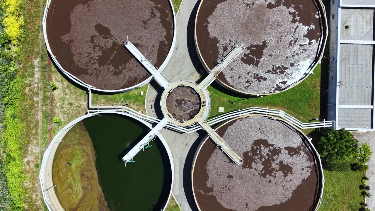 Vista de una planta de tratamiento de agua con tanques circulares que muestran las diferentes etapas del procesamiento de residuos y el sistema de tratamiento, tomada desde arriba durante el día.