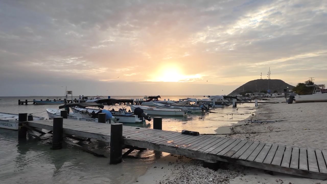 Træmole og både langs sandstrand ved solnedgang, fredfyldt caribisk ø-scene