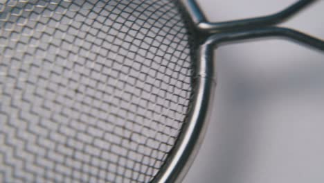 metal-strainer-with-long-handle-lies-on-white-surface-macro