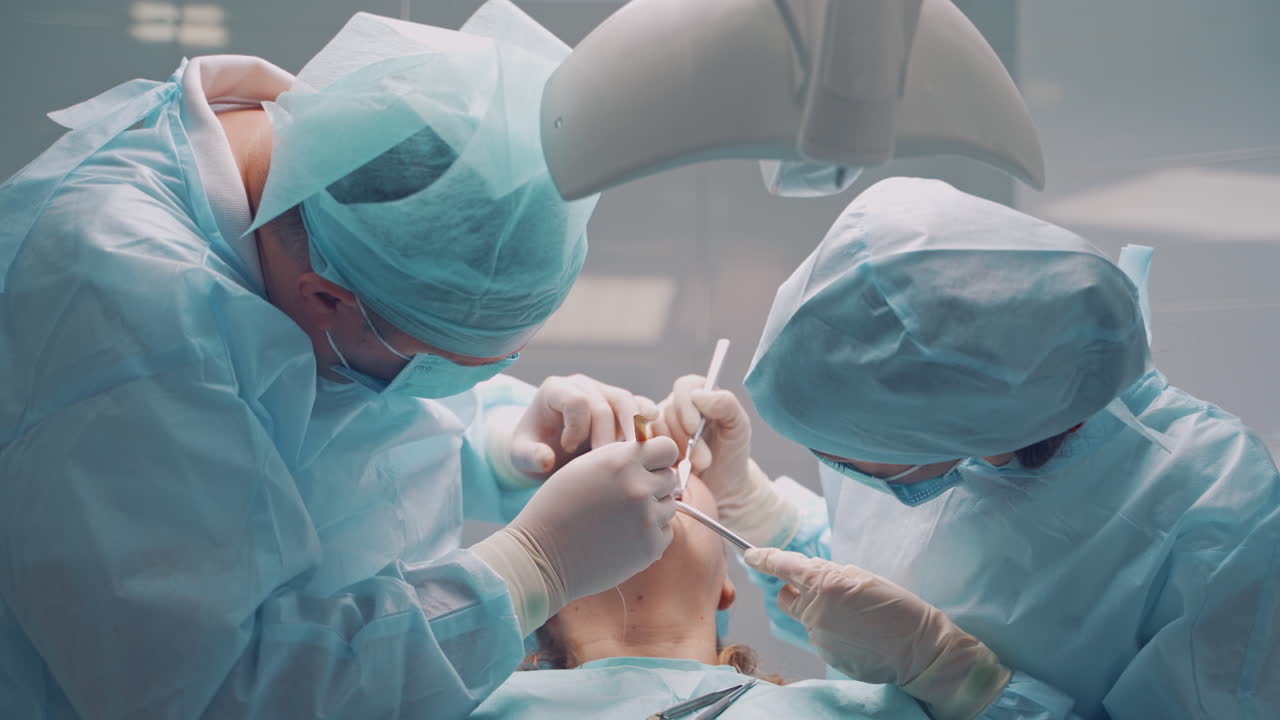 A male dentist in uniform perform dental implantation operation on a patient at dentistry office.