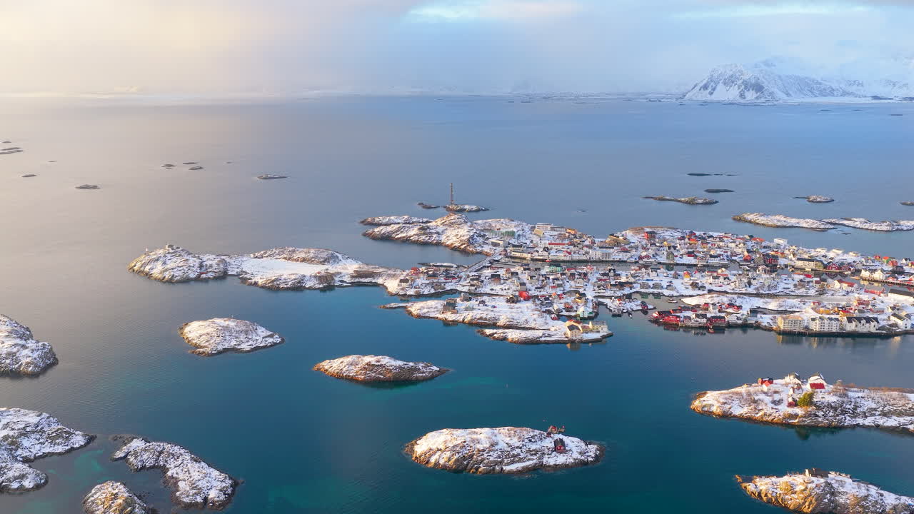 Filmatisk luftfoto av det berømte fiskeværet Henningsvær omgitt av iskalde blå arktiske farvann og snødekte øyer i Lofoten, Norge